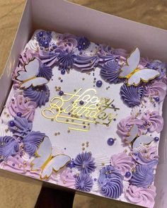 a birthday cake in a box with purple frosting and butterflies on the top, sitting on a table