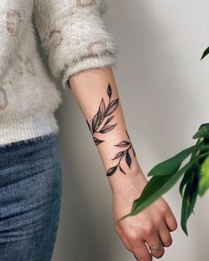 a woman's arm with a black leaf tattoo on the left wrist and an olive branch in the middle