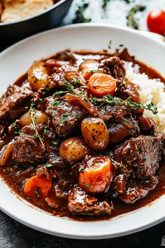 a white plate topped with beef and potatoes covered in gravy on top of rice