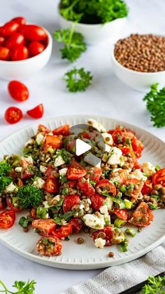 a white plate topped with salad next to bowls of tomatoes