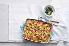 a casserole dish with noodles and vegetables in it on a white tablecloth