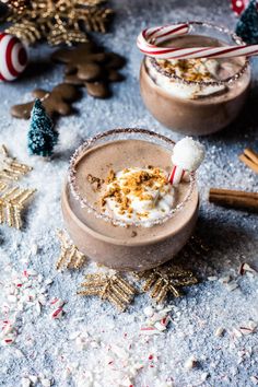 two glasses filled with hot chocolate and marshmallows on top of snow covered ground