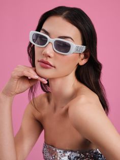 a woman wearing sunglasses and posing for the camera with her hand on her chin, in front of a pink background