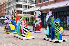 several colorful sculptures are on display in the middle of a brick street with tall buildings behind them