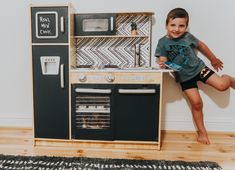 a young boy standing next to a toy stove and oven in front of a wall