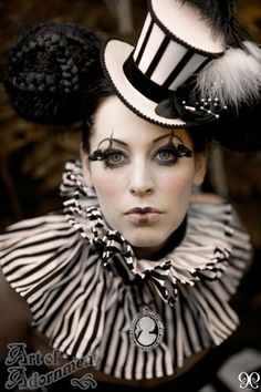 a woman with black and white makeup wearing a top hat, striped dress and feathered headdress