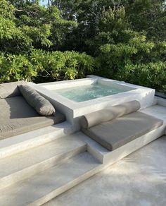 a hot tub sitting on top of a cement patio next to trees and bushes in the background