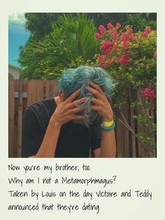 a person with blue hair covering their face in front of a fence and pink flowers