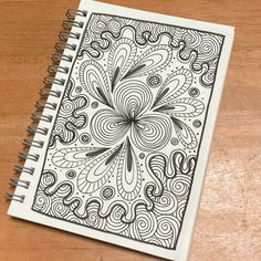 a spiral notebook with an intricate design on the front and back cover, sitting on a wooden surface