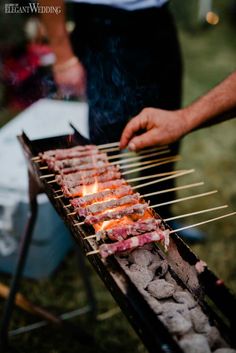 a man is cooking on an outdoor grill with skewers filled with meat and vegetables