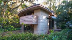 a small wooden building in the middle of some bushes and trees with lots of greenery around it