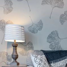 a lamp on a table next to a couch with a blue pillow and wallpaper