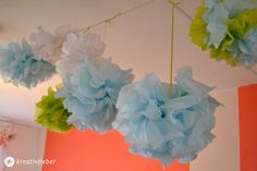 blue and green paper flowers hanging from the ceiling in a room with orange walls,