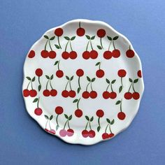 a white plate with cherries on it against a blue background that is painted in red and green