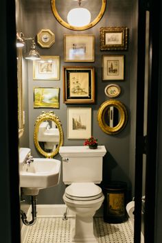 a white toilet sitting in a bathroom next to a sink and framed pictures on the wall