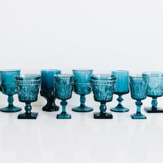 blue glass goblets are lined up on a white surface, with one in the middle