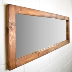 a mirror mounted to the side of a white brick wall next to a wooden frame