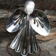 a metal sculpture with spoons on top of it in front of a stone wall