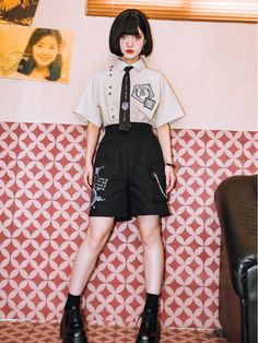 a woman standing in front of a wall wearing black shorts and a white t - shirt