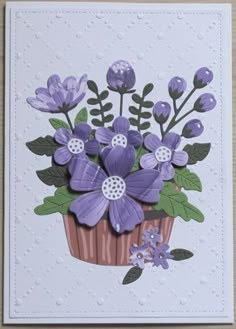 a card with purple flowers and green leaves in a cupcake style vase on a table