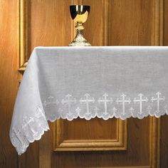 a white table cloth with a cross on it and a cup in front of it