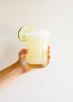 a person holding up a glass with a lime and ice in it, on a white background