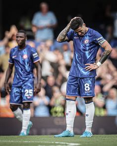 two soccer players are standing on the field with their hands in their hair and one is holding his head