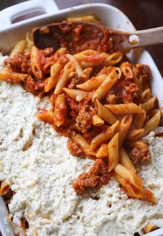 pasta and sauce in a casserole dish with a wooden spoon on the side