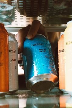 a person is holding a can of soda in front of several other cans on the counter