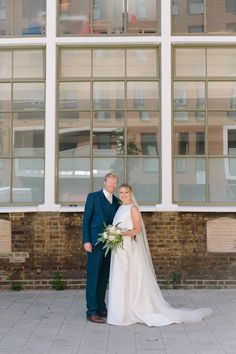 a bride and groom standing in front of a building with large windows on each side