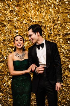 a man and woman standing next to each other in front of a gold foil wall