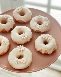 six glazed donuts with white frosting and daisies on a pink platter