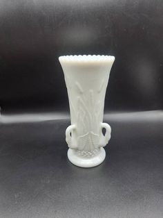 a white glass vase sitting on top of a table next to a black countertop