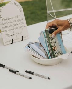 a person holding magazines on top of a white table next to a sign that says, find a postcard of places that are special to the couple & write your memory or advice