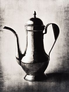 an antique silver tea pot with a spoon in the handle, on a gray background