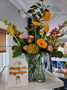 a vase filled with lots of flowers on top of a white counter next to a sign