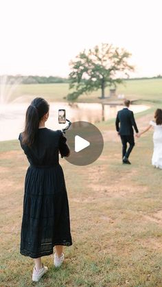 a woman in a black dress taking a photo with her cell phone while two other people walk by