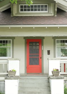 a red door sits in front of a white house with two planters on the steps