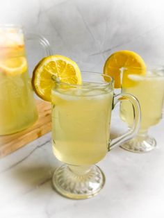 two glasses filled with lemonade sitting on top of a table next to a cutting board