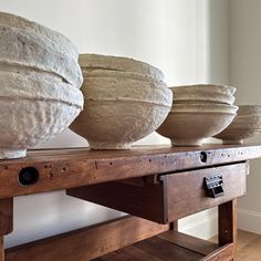 three large stone bowls sitting on top of a wooden table next to each other in front of a white wall