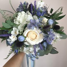 a blue vase with white flowers and greenery on the top is held by someone's hand