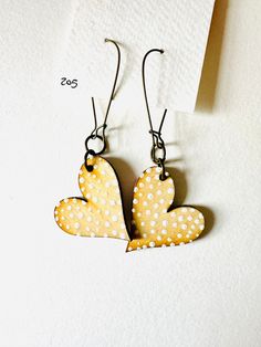 two heart shaped wooden earrings hanging from hooks on a white surface with small polka dots