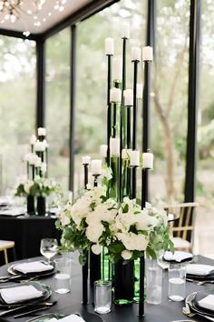 a black table with white flowers and candles on it in front of a large window