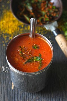 a metal pot filled with red sauce next to a wooden spoon