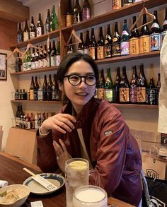 a woman sitting at a table with lots of bottles on the wall behind her and plates in front of her