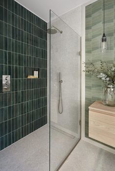 a bathroom with a glass shower door and green tile on the wall, next to a wooden counter