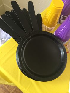 black paper plates and purple plastic cups on a yellow table cloth