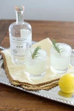 two glasses on a tray with lemon and rosemary garnish next to a bottle of gin