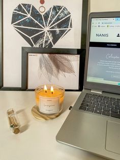 a laptop computer sitting on top of a desk next to a candle and some pictures