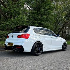 the rear end of a white bmw car parked in front of some trees and bushes